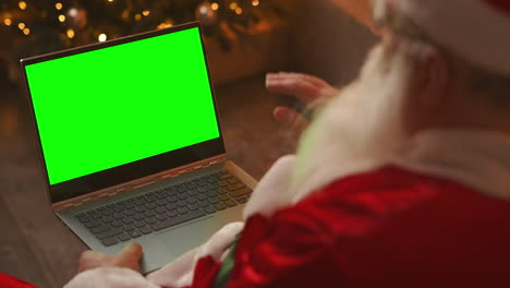 Papá-Noel-Está-Hablando-En-Una-Videollamada-A-Través-De-Una-Computadora-Portátil.-Utilice-La-Pantalla-Verde-Para-Una-Videollamada.-Papá-Noel-Saluda-Con-La-Mano-Mirando-La-Pantalla-Verde-Del-Portátil.-Imágenes-4k-De-Alta-Calidad