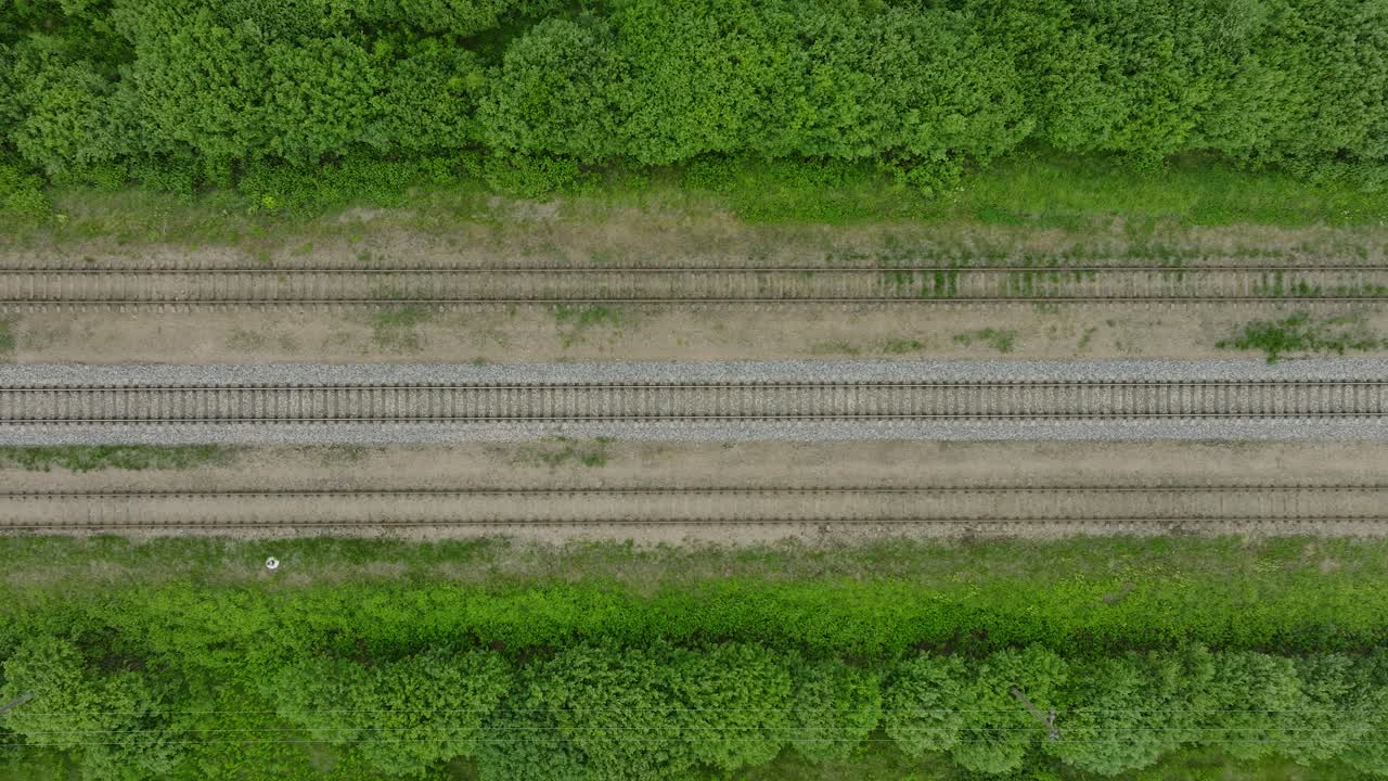 Aerial birdseye view of empty railroad train tracks, countryside scenery, fresh green forest on the side, overcast cloudy summer day, wide drone dolly shot moving left