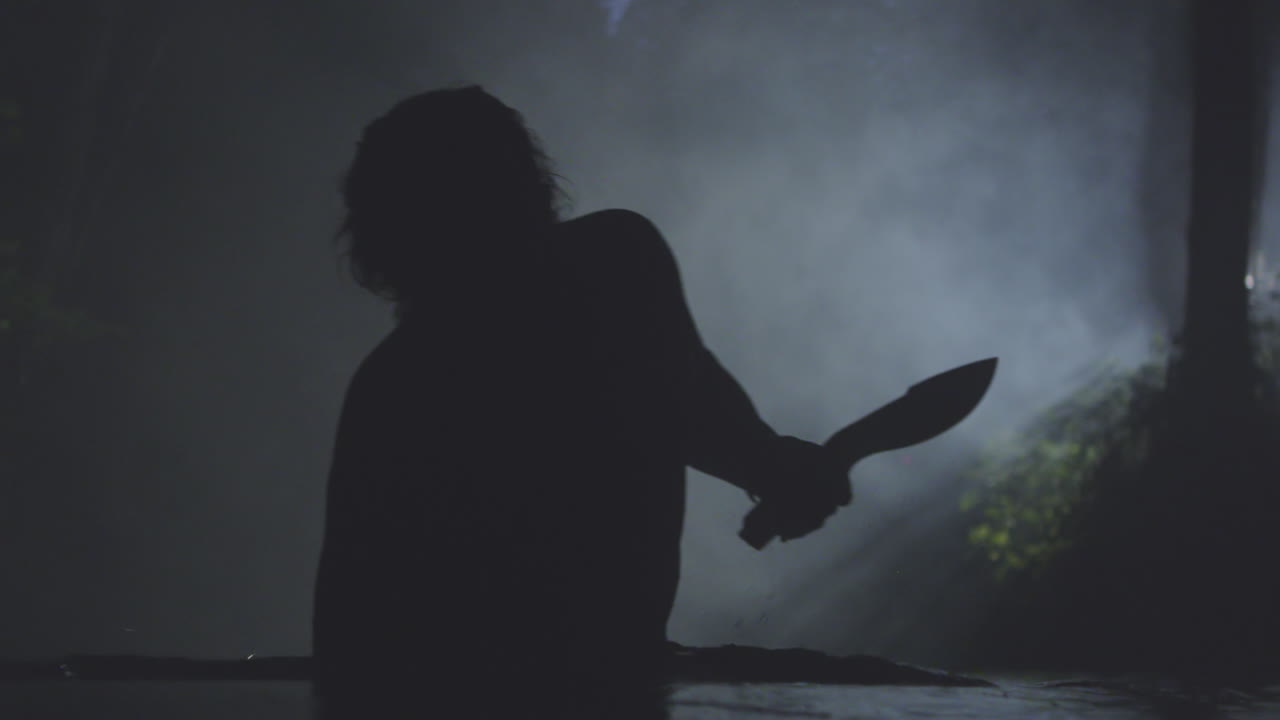 A man walking water in a dark cave while carrying a knife
