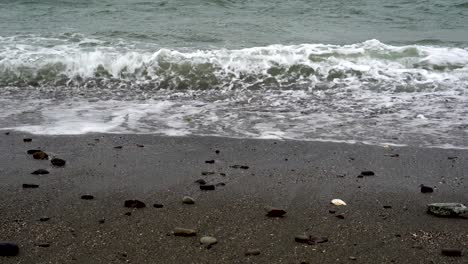 Close-up-of-ocean-waves-breaking-on-beach-with-scattered-rocks-pebbles