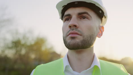 close-up portrait of a male engineer or construction worker in a hard hat and safety vest looking upwards outdoors