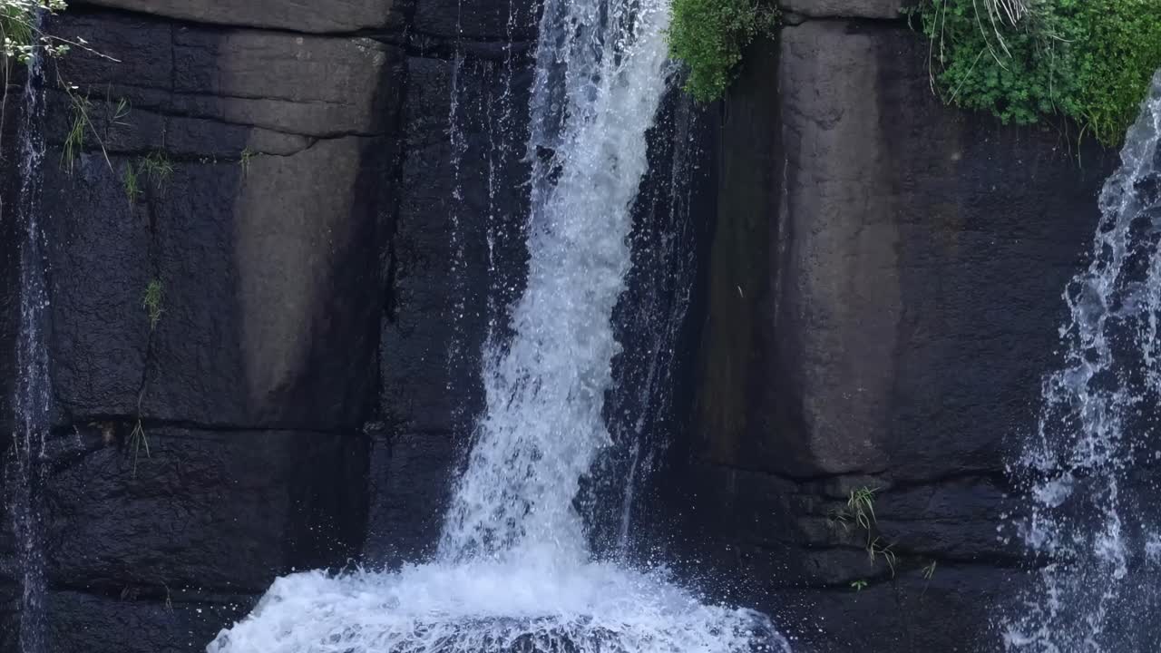A detailed view of water cascading down a rugged cliff face with lush greenery.