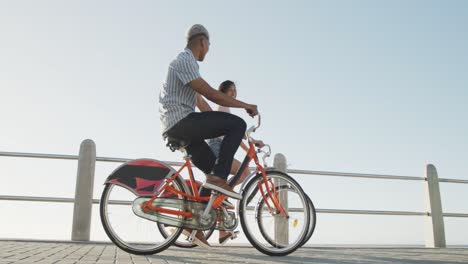 happy biracial couple riding bikes on promenade, in slow motion