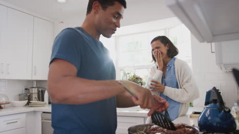 Young-African-American-couple-talking-in-the-kitchen,-man-cooking-food-on-the-hob,-close-up,-side-view