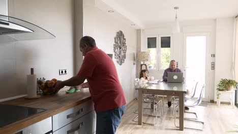 domestic scene of a mature man cleaning while family sits on a table