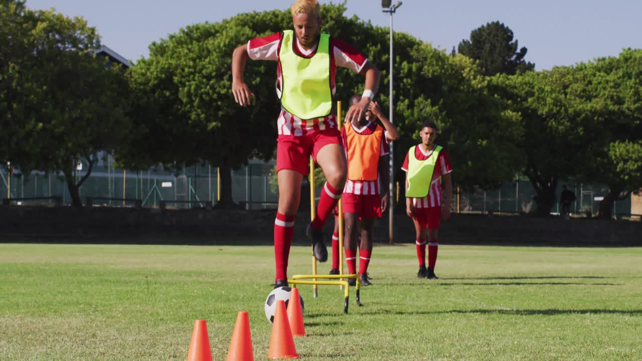 Video of diverse group of male football players warming up on field, running and kicking ball