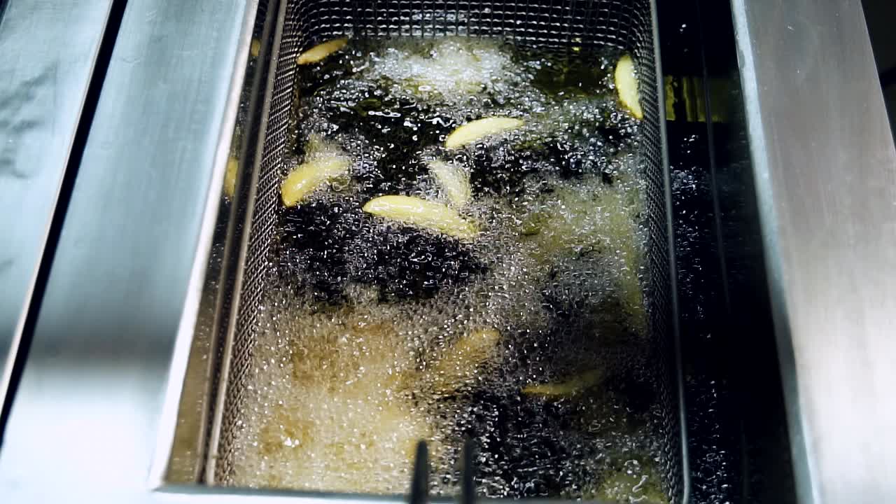 Cooking and frying french fries in oil. Boiling deep fat in a large bowl on the stove in a restaurant. Slow motion
