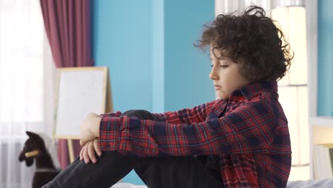 el niño triste está sentado en la cama de la habitación.