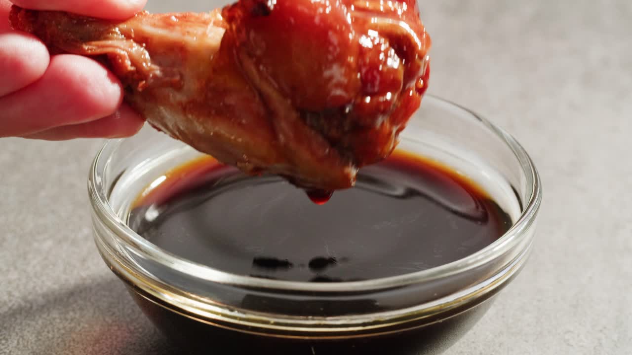 Hand Dipping a Glazed Chicken Wing in Sauce