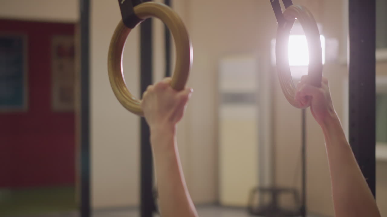 Asian woman reaching for gym rings, crossfit athlete warming up under studio lights, trainerlike focus on grip and shoulder engagement, evening practice captures determination and controlled motion