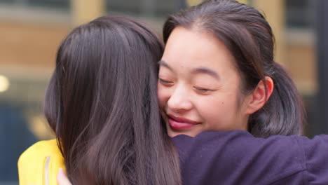 close up of two smiling young female friends meeting and hugging in urban setting together 4