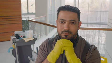 close up view of arabic cleaning man wearing headphones posing at camera while holding a mop stick