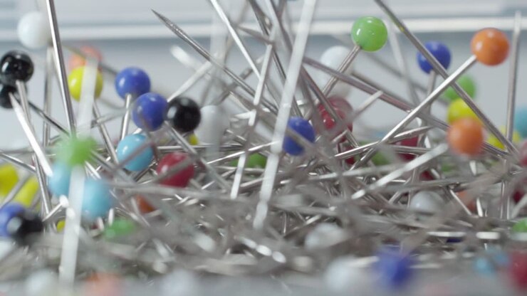 Pan left shot of colorful metallic sewing pins with round heads inside transparent plastic container