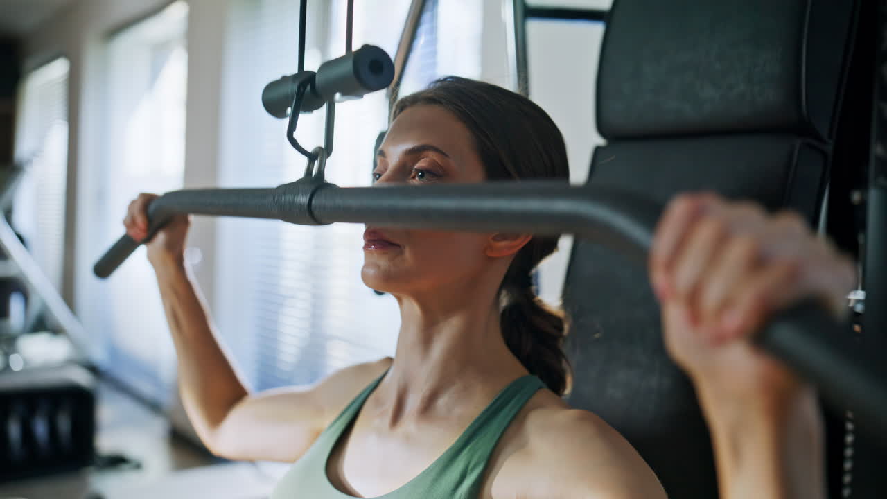 Woman performing lat pulldown in gym closeup. Portrait athlete training hands