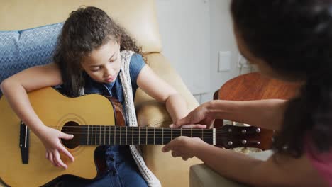 happy mixed race mother and daughter playing with guitar