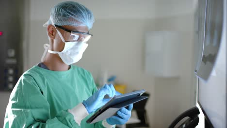 Serious-asian-male-surgeon-with-face-mask-using-tablet-in-operating-room-in-slow-motion