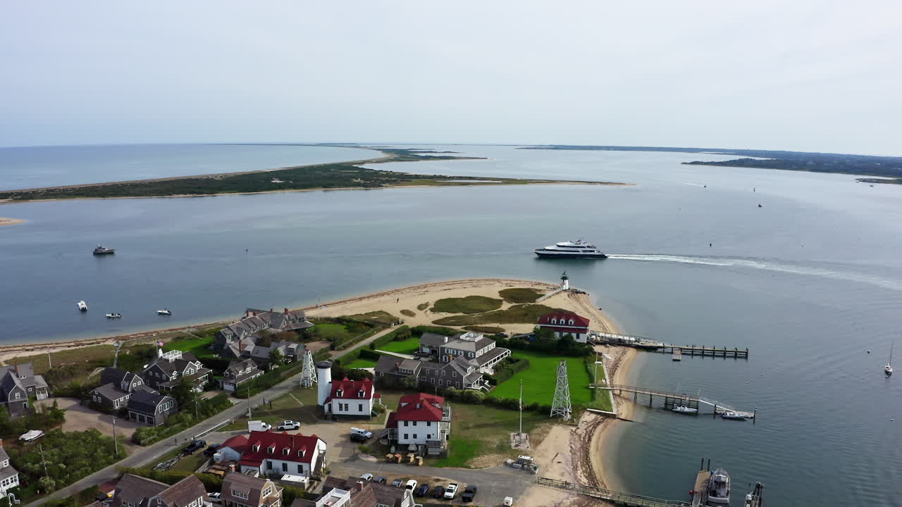Um drone sobrevoa o Farol Brant Point em Nantucket, Massachusetts, enquanto uma balsa desliza pelo porto, revelando a península, casas costeiras e a costa em camadas vistas de cima.