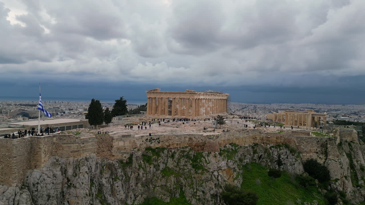 A drone captures the Acropolis with tourists below in February. The pleasant weather features a slightly cloudy sky, adding to the picturesque view of this iconic Greek landmark.