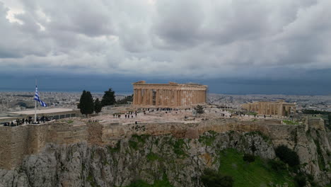a drone captures the acropolis with tourists below in february. the pleasant weather features a slightly cloudy sky, adding to the picturesque view of this iconic greek landmark.