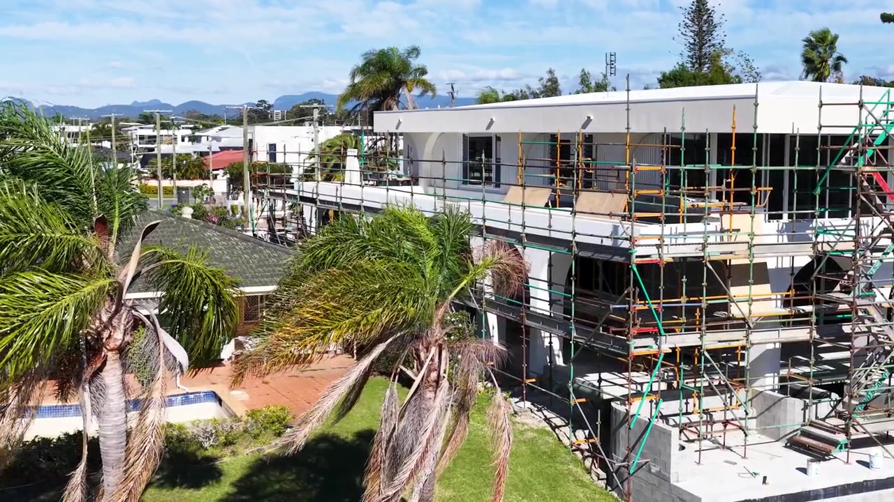 Static wide shot of a modern white house undergoing renovation with scaffolding under bright sunlight.