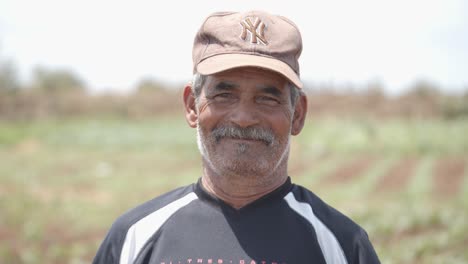 a farmer wearing a hat is standing in the middle of his field, looking at the camera and smiling