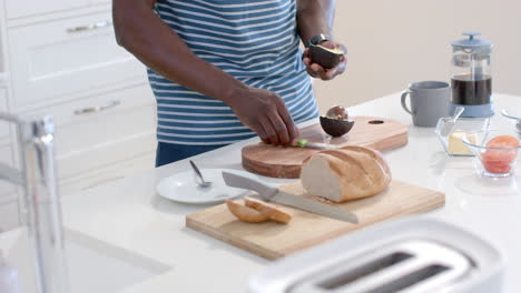 african american man preparing avocado toasts in sunny kitchen, slow motion