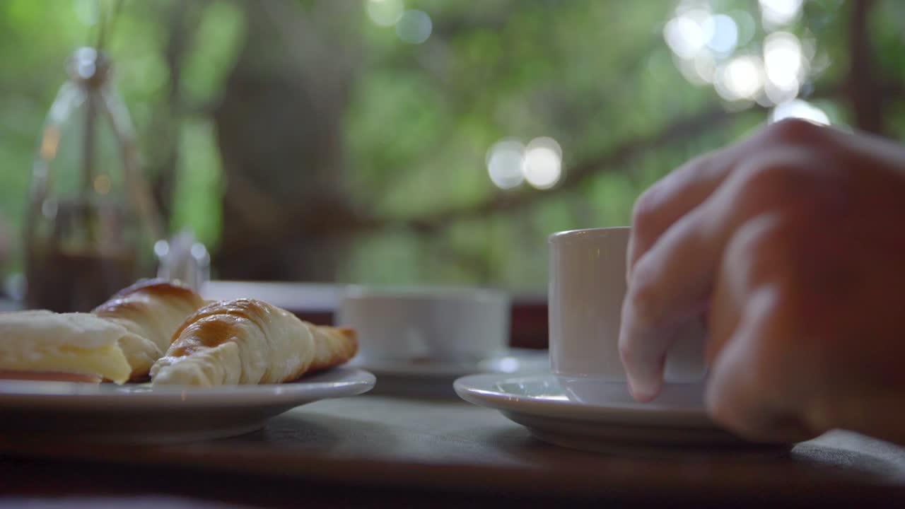 manos recogiendo una taza de café de una mesa de desayuno y luego colocándola de nuevo en el mismo lugar