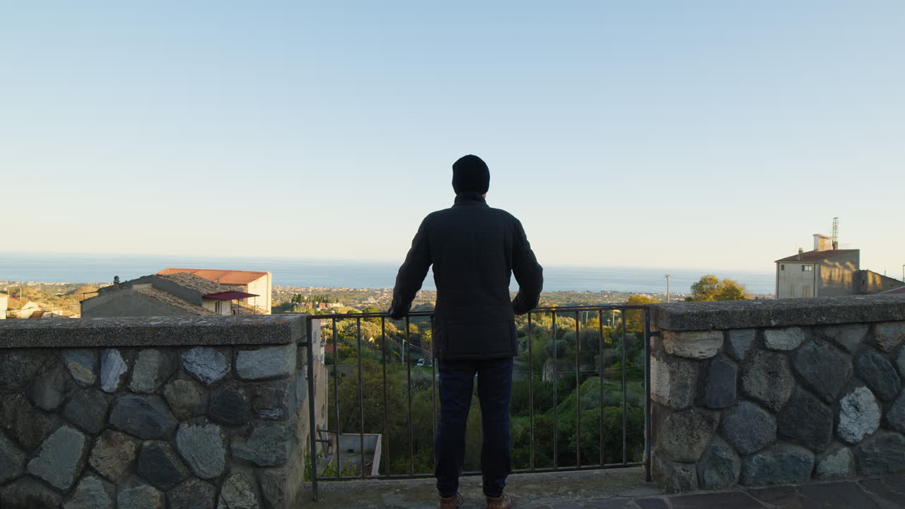한 남자의 실루이 도시의 발코니에서 바다를 바라보고 있습니다.