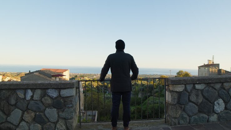 Silhouette Of A Man Looks Out From The Balcony Of The City And Observes The Sea