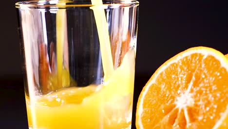 close-up of fresh orange juice being poured into a glass beside a sliced orange.