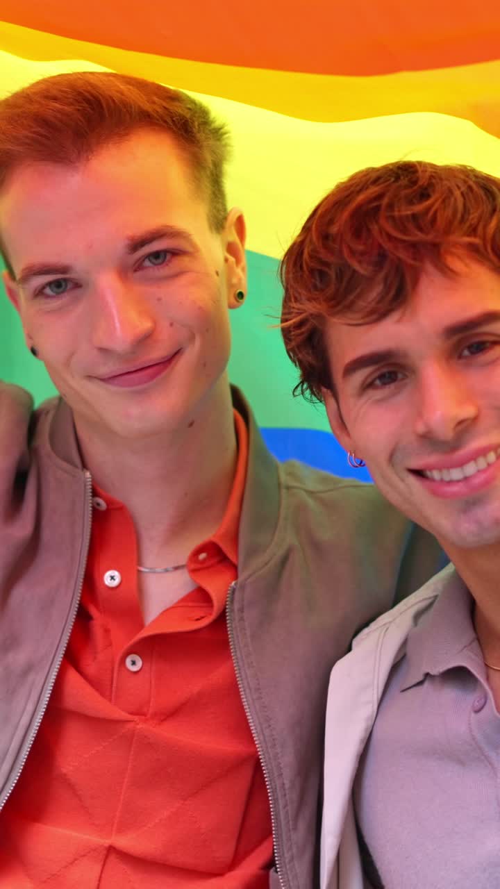Coppia gay felice che sorride sotto la bandiera arcobaleno del Pride
