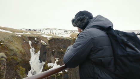 Middle-Age-Man-Standing-on-Viewpoint-Platform-Above-Canyon-in-Cold-Icelandic-Landscape
