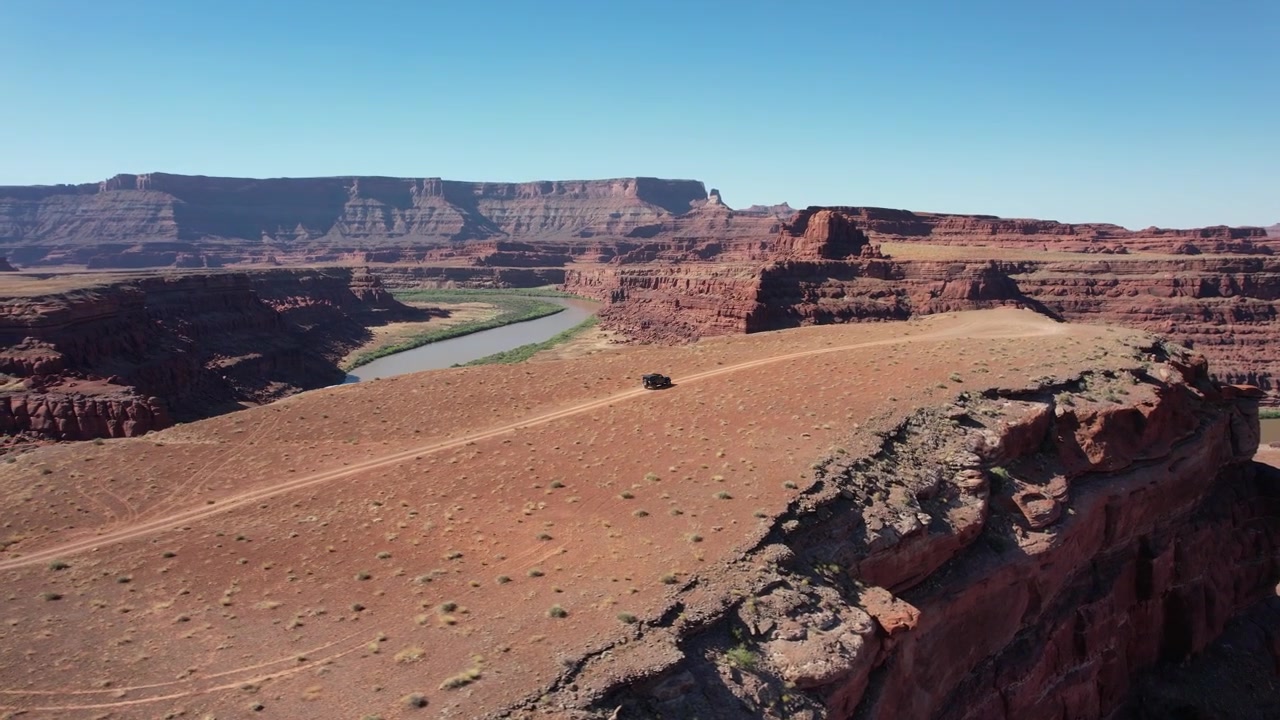 Drone in volo circolare mentre un fuoristrada percorre una strada sterrata verso il bordo di una scogliera a Moab, USA, in 4K.