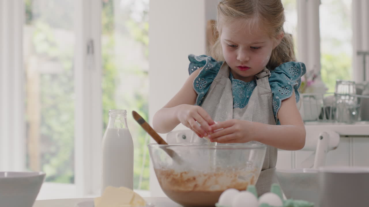 niña feliz horneando en la cocina mezclando ingredientes para la masa de galletas casera rompiendo huevos en el cuenco divirtiéndose preparando deliciosas golosinas para el desayuno en casa 4k metraje