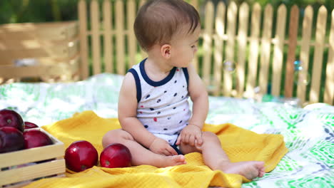 little baby boy watching the soap bubbles fly. cute calm caucasian child sitting in the garden in summer. blurred backdrop.