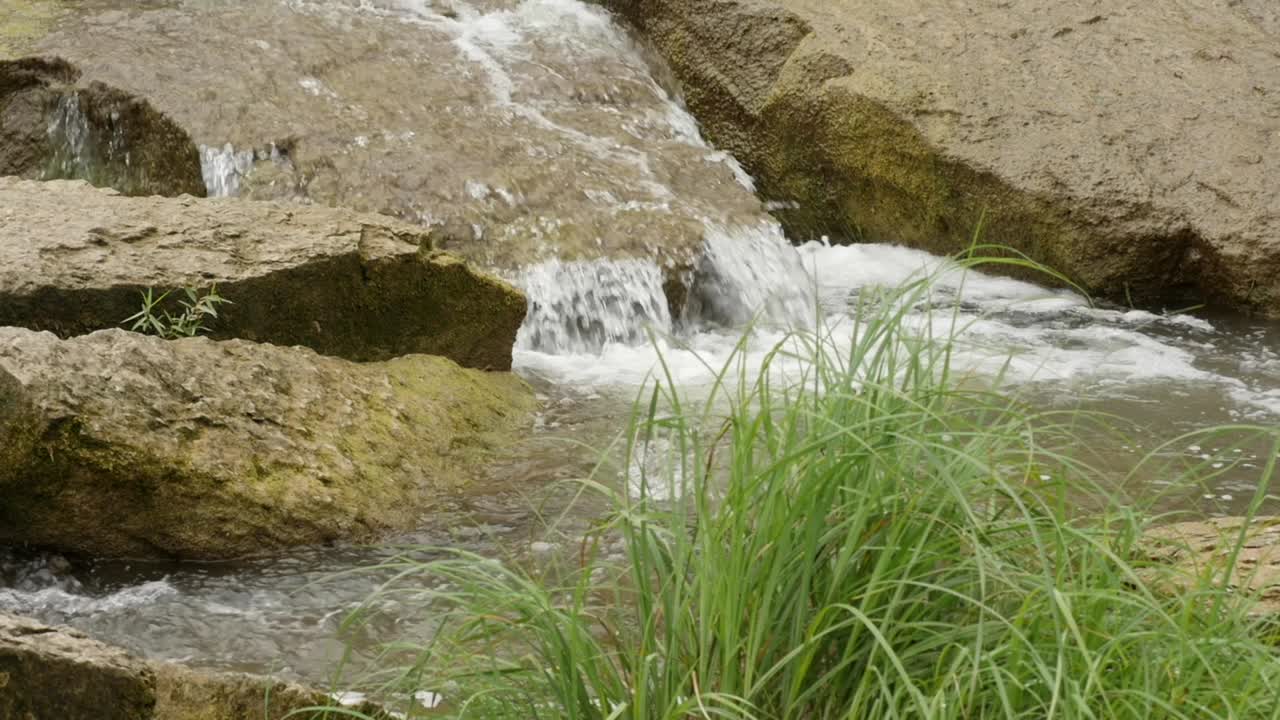 una corriente de agua dulce clara y poco profunda fluye sobre las rocas en un día soleado, cierra en cámara lenta estática