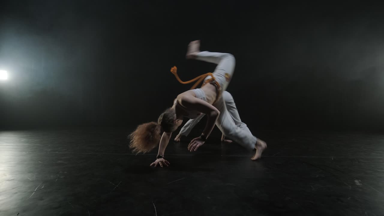 Gruppo di ballerini professionisti che praticano capoeira nell'oscurità contro un riflettore su uno sfondo nero dello studio. Arte marziale afro-brasiliana che combina elementi di danza