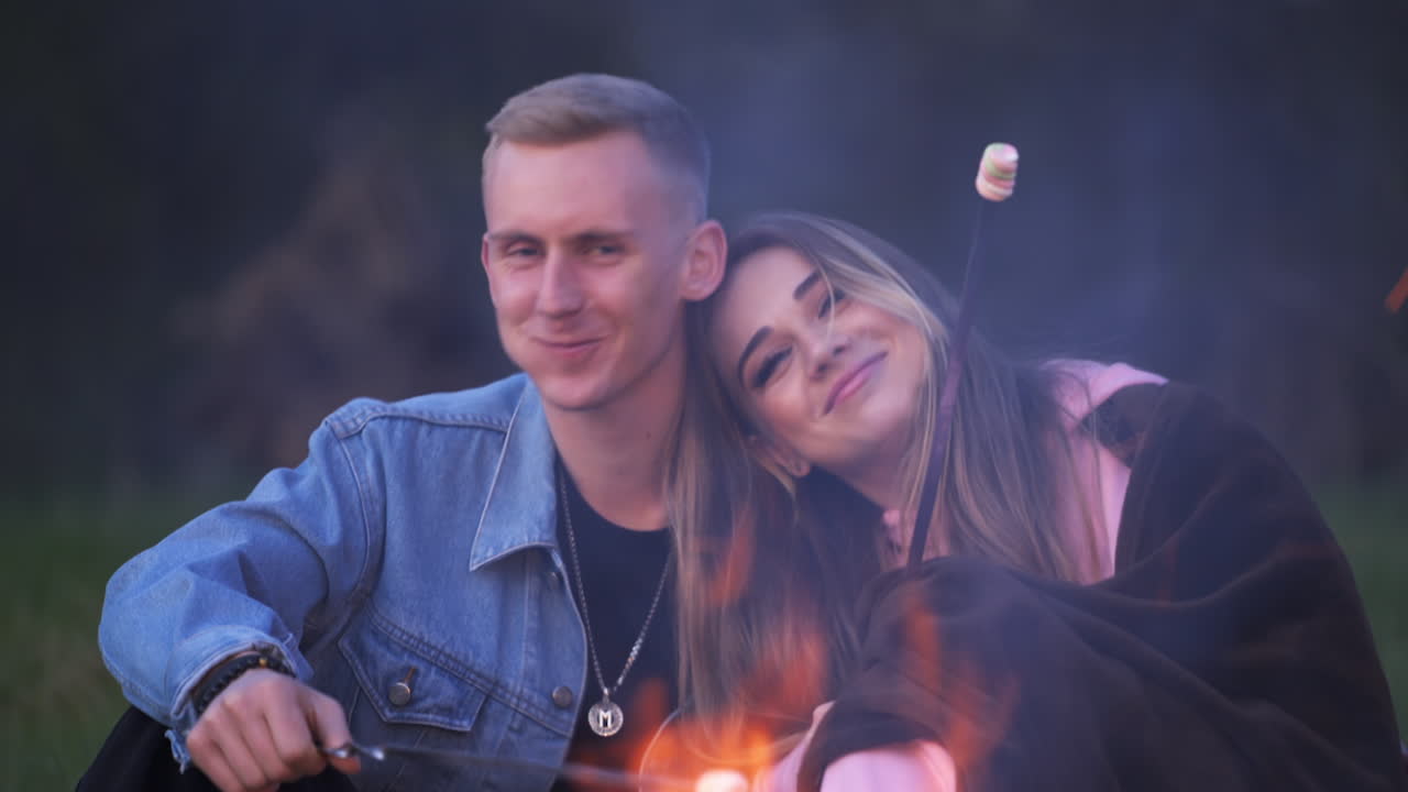 Couple in love having fun at picnic. Young pair holding marshmallows in the bonfire. Female feeding her boyfriend with marshmallow.