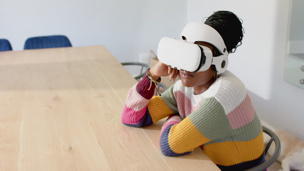 Using VR headset, woman sitting at wooden table in colorful sweater