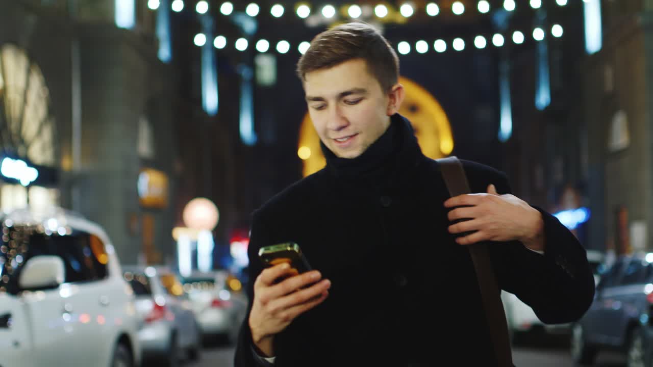 젊은 남자가 밤 도시를 걷고 스마트폰을 사용합니다