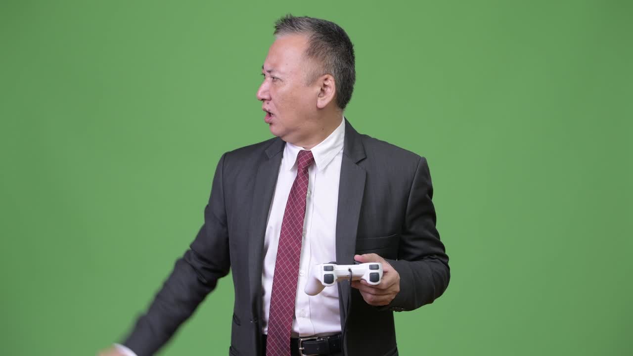 성숙 한 일본인 사업가 가 초록색 배경 에 게임 을 하고 있다