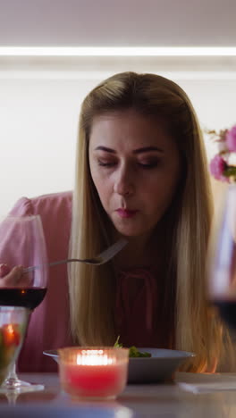 attractive lady eats juicy vegetarian salad sitting at served table with flowers bouquet and burning candle at festive dinner in kitchen slow motion