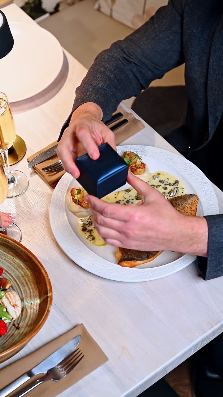 Romantic dinner with proposal and ring box at a restaurant table. Two people share a meal at a restaurant. One person holds a ring box while the other looks surprised
