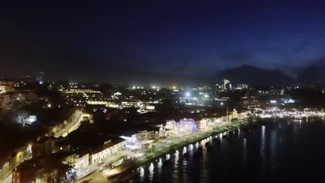 Nach-Unten-Neigende-Luftaufnahme-Von-Gaia-Bei-Nacht-Entlang-Des-Flussufers,-Portugal