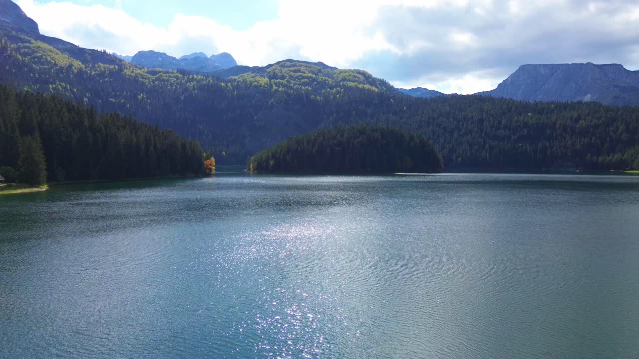 Black Lake in Durmitor National Park surrounded by dense coniferous forests with mountain backdrop in sunny daylight, Aerial