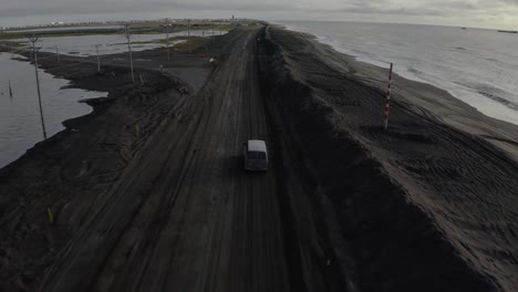 Toma-Aérea-De-Un-Dron-De-Una-Camioneta-Conduciendo-A-Lo-Largo-De-Una-Carretera-Inundada-Junto-Al-Océano-Ártico-Cerca-De-Barrow-Alaska