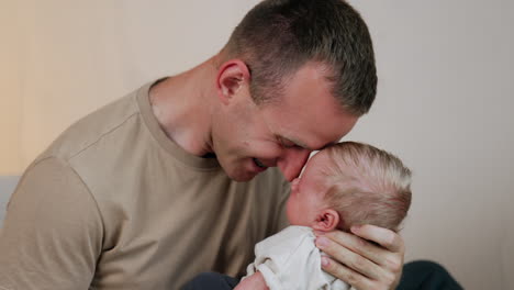 happy smiling dad leans to the newborn he's holding in his hands. father spending time with baby.
