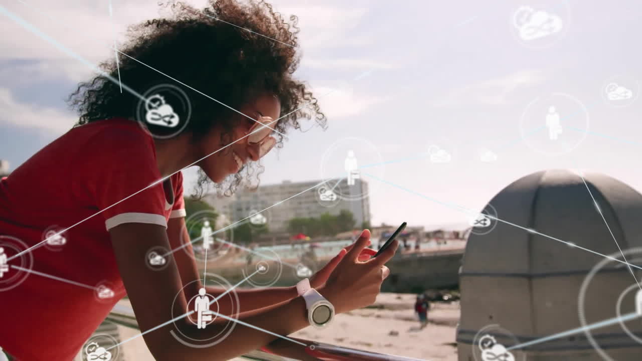 Animation of network of connections with icons over biracial woman using smartphone by sea
