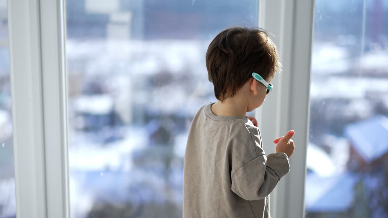 A little boy looks out the window at the snow