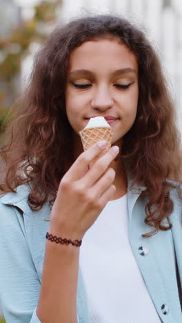 happy pretty preteen child kid girl standing eating tasty ice cream in waffle cup in urban city